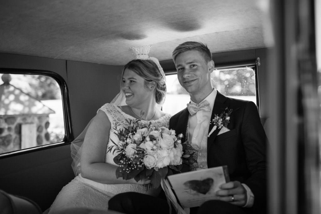 Svartvit bild på brudpar i bil efter vigseln. Foto: Tove Lundquist, bröllopsfotograf Sverige.