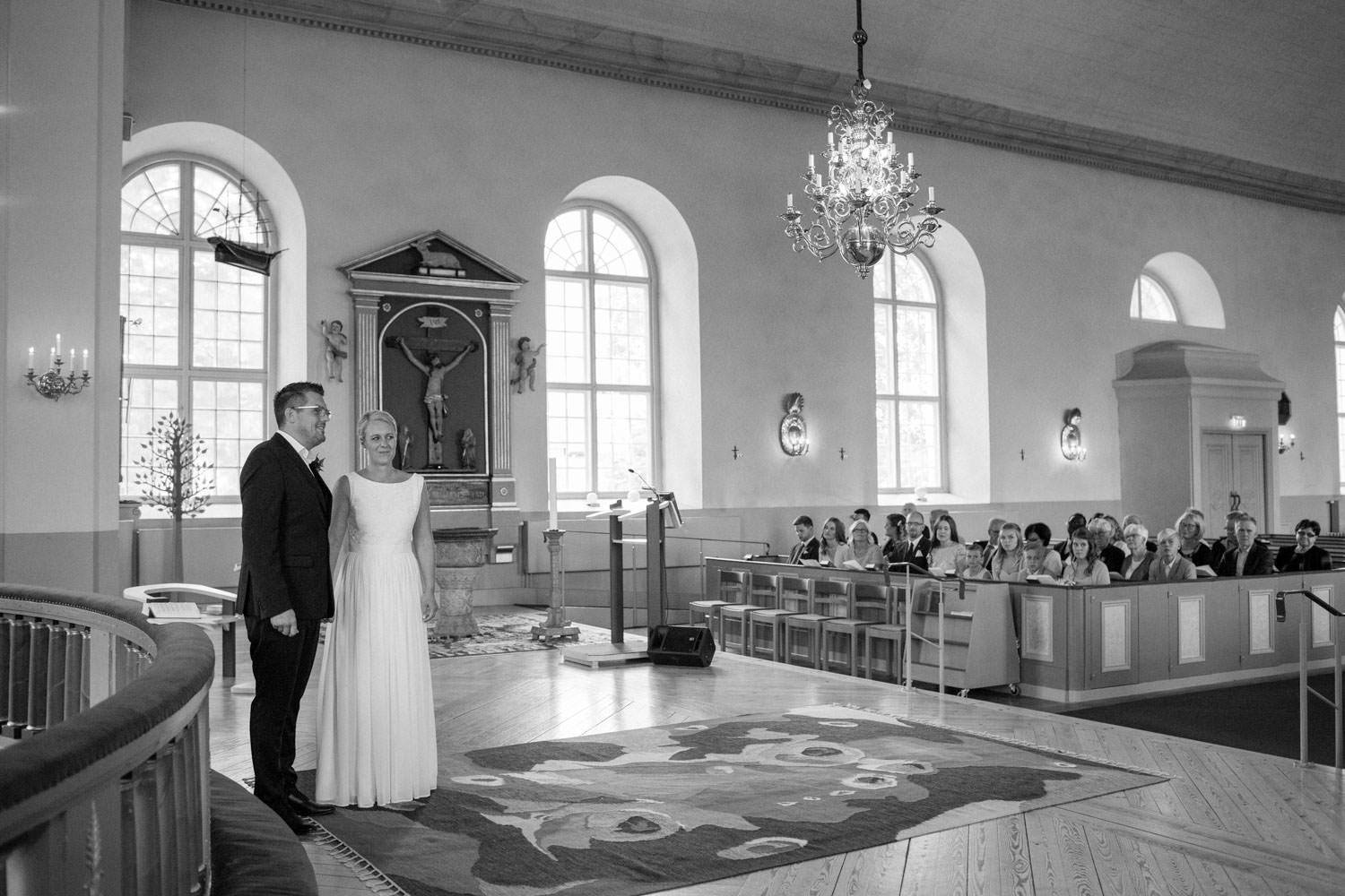 Svartvitt foto på brudpar som gifter sig i Mönsterås kyrka. Brudgummens kostym kommer från Dressmann. Brudens klänning kommer från Sofia Moore.