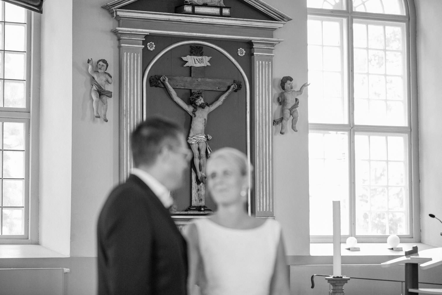 Svartvitt foto på brudpar som gifter sig i Mönsterås kyrka. Bröllopsfotograf är Tove Lundquist. Brudgummens kostym kommer från Dressmann. Brudens klänning kommer från Sofia Moore.