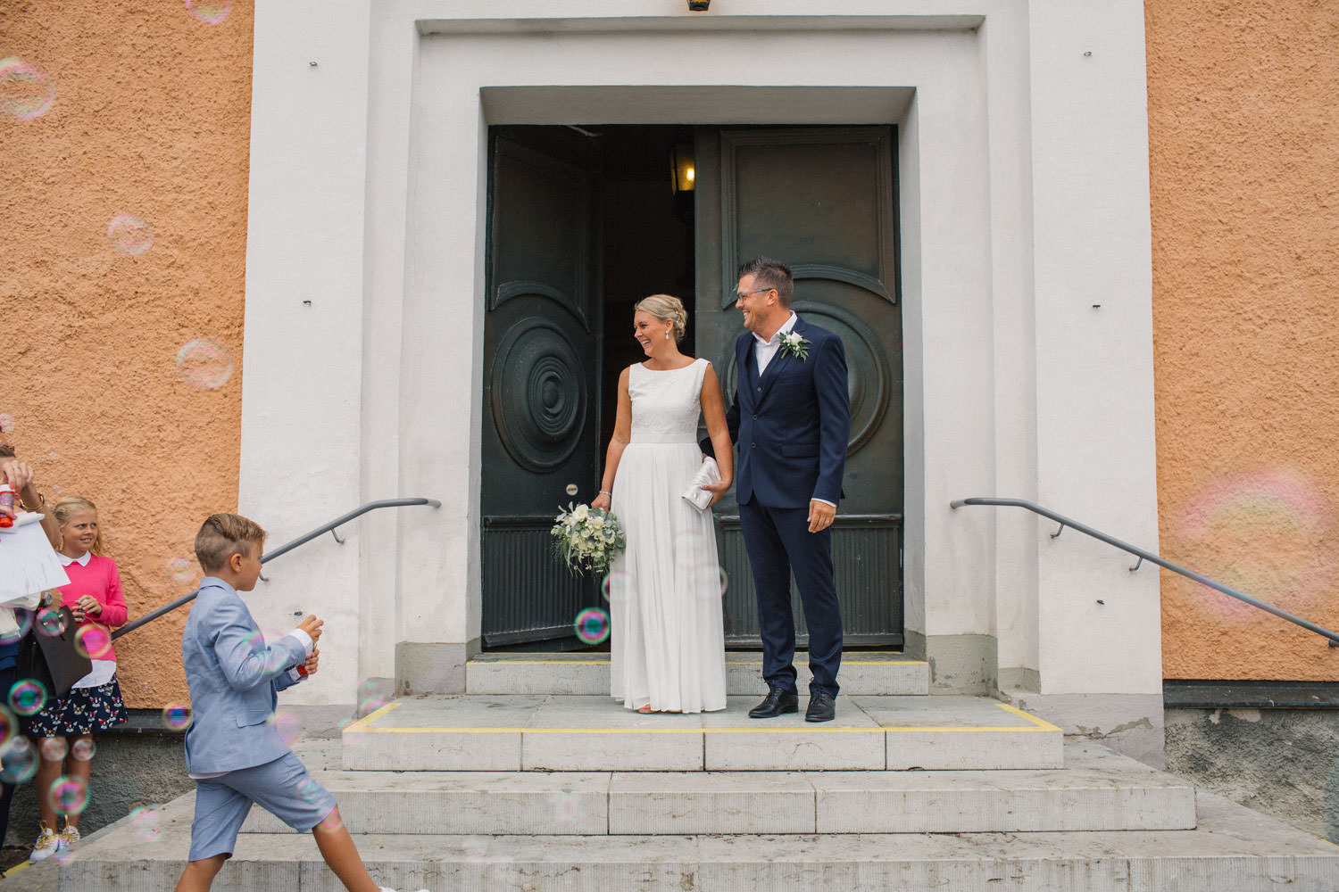 Brudpar står utanför kyrkan tillsammans med sina gäster, bröllop i Mönsterås.