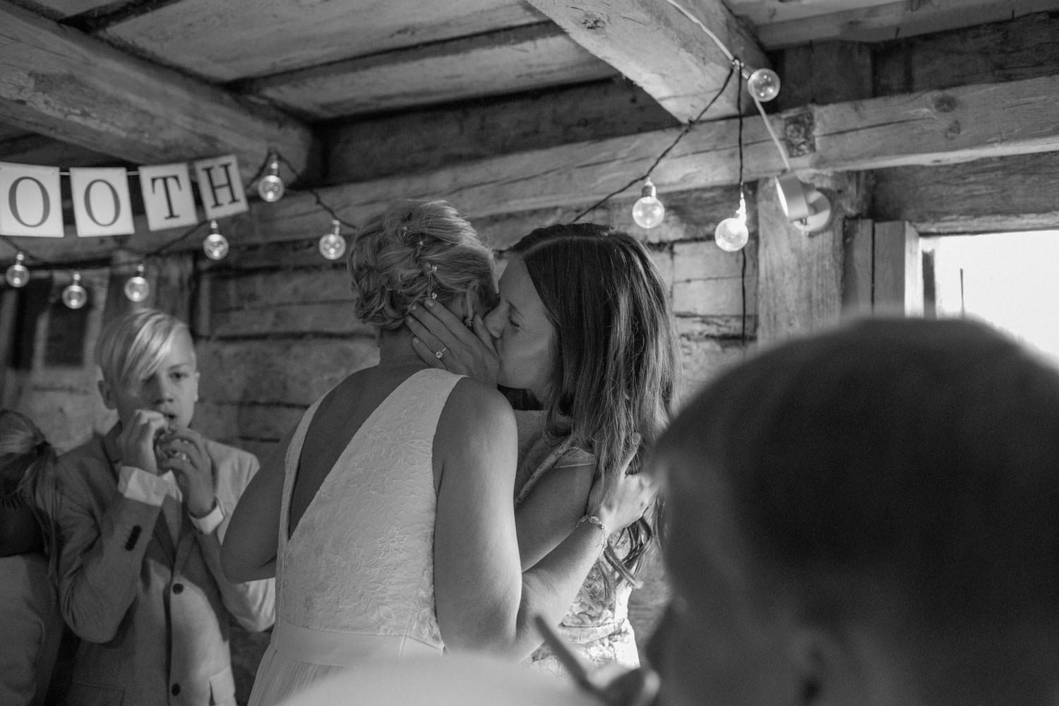 Svartvitt foto på svägerska som pussar bruden i ett Photo Booth. Plats är Kaffetorpet Oknö, Småland.