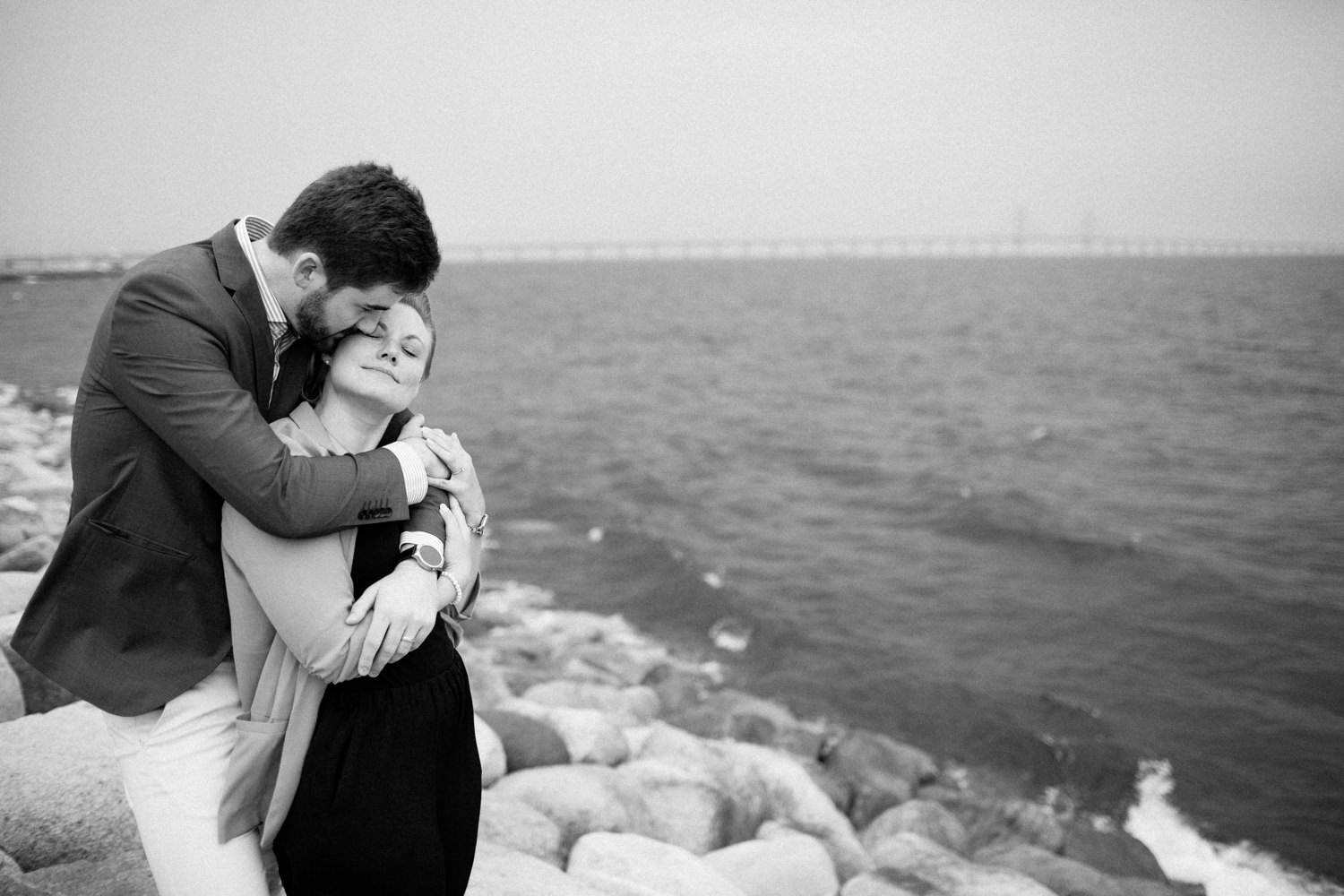 Kärleksfull bild från en parfotografering med förlovat par, Ön Limhamn i Malmö. Fotograf är Tove Lundquist, platsen är Ön, Limhamn i Malmö. Öresundsbron i bakgrunden. 