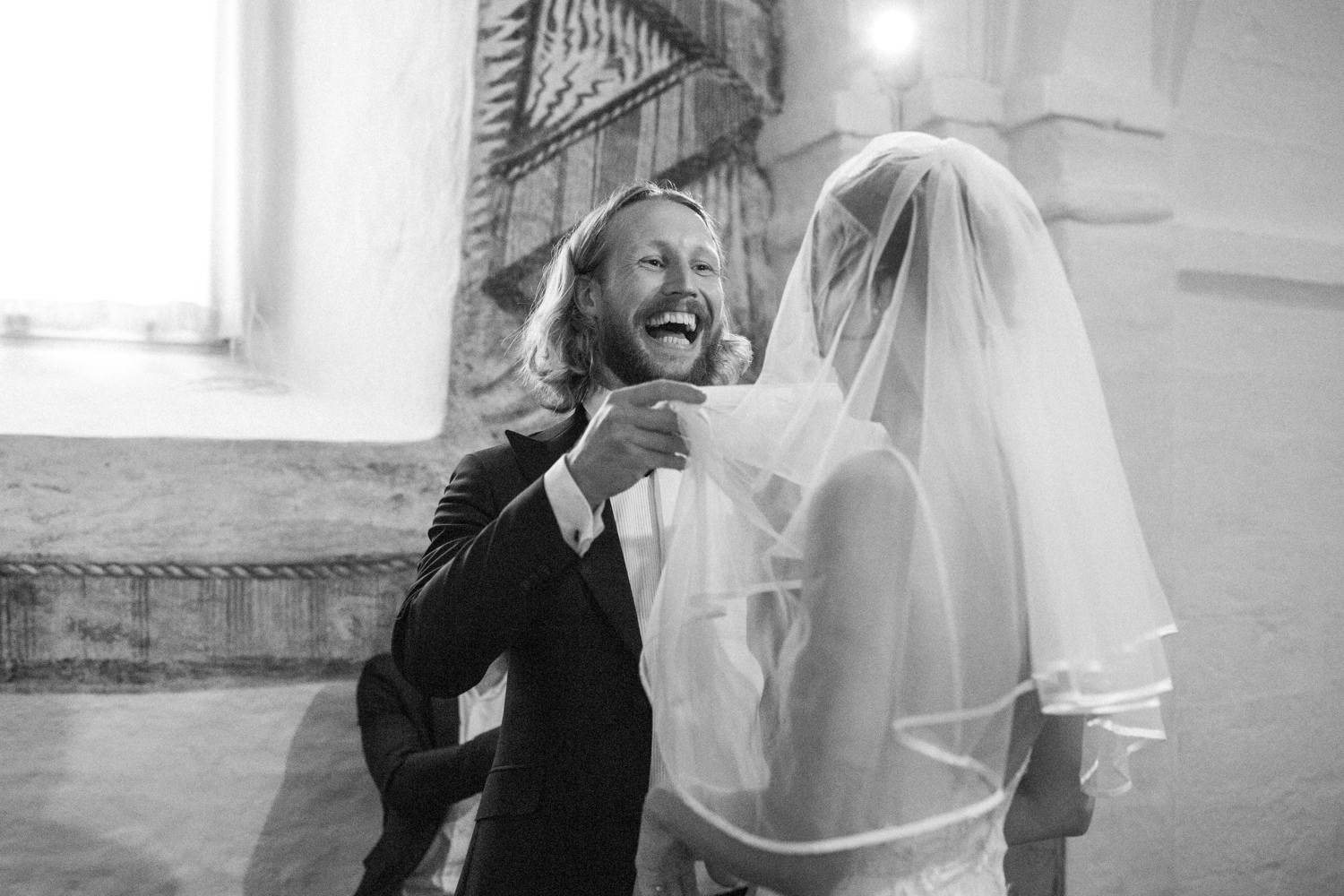 Svartvitt porträtt på brudgum som skrattar under vigseln, från ett bröllop i Göteborg, Västra Götaland. Foto: Tove Lundquist, bröllopsfotograf.