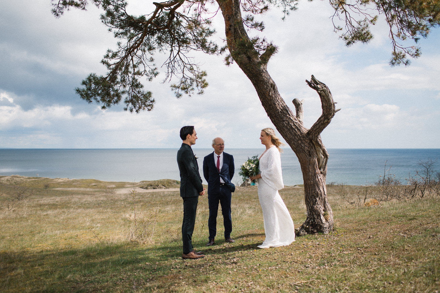 Foto på brudpar vid ett ringbyte under ett elopement bröllop i Haväng, Skåne. Bilder från vigseln vid den ensamma tallen. Fotograf: Tove Lundquist.