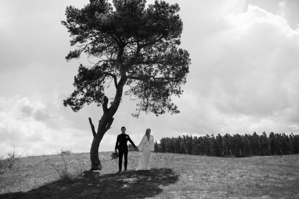 Svartvitt fotografi på brudpar under det ensamma trädet i Haväng där deras utomhusvigsel skedde. Paret hade planerat ett elopement bröllop i Skåne. Bröllopskläder: Tiger of Sweden samt Asos. Bröllopsfotograf är Tove Lundquist.