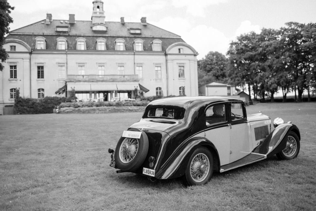 Svartvitt fotografi på brudparets hyrda veteranbil vid ett bröllop på Örenäs Slott i Skåne.